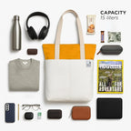 The Skylin tote bag in off-white and yellow, surrounded by a water bottle, headphones, and essential items, showcasing its modern design.