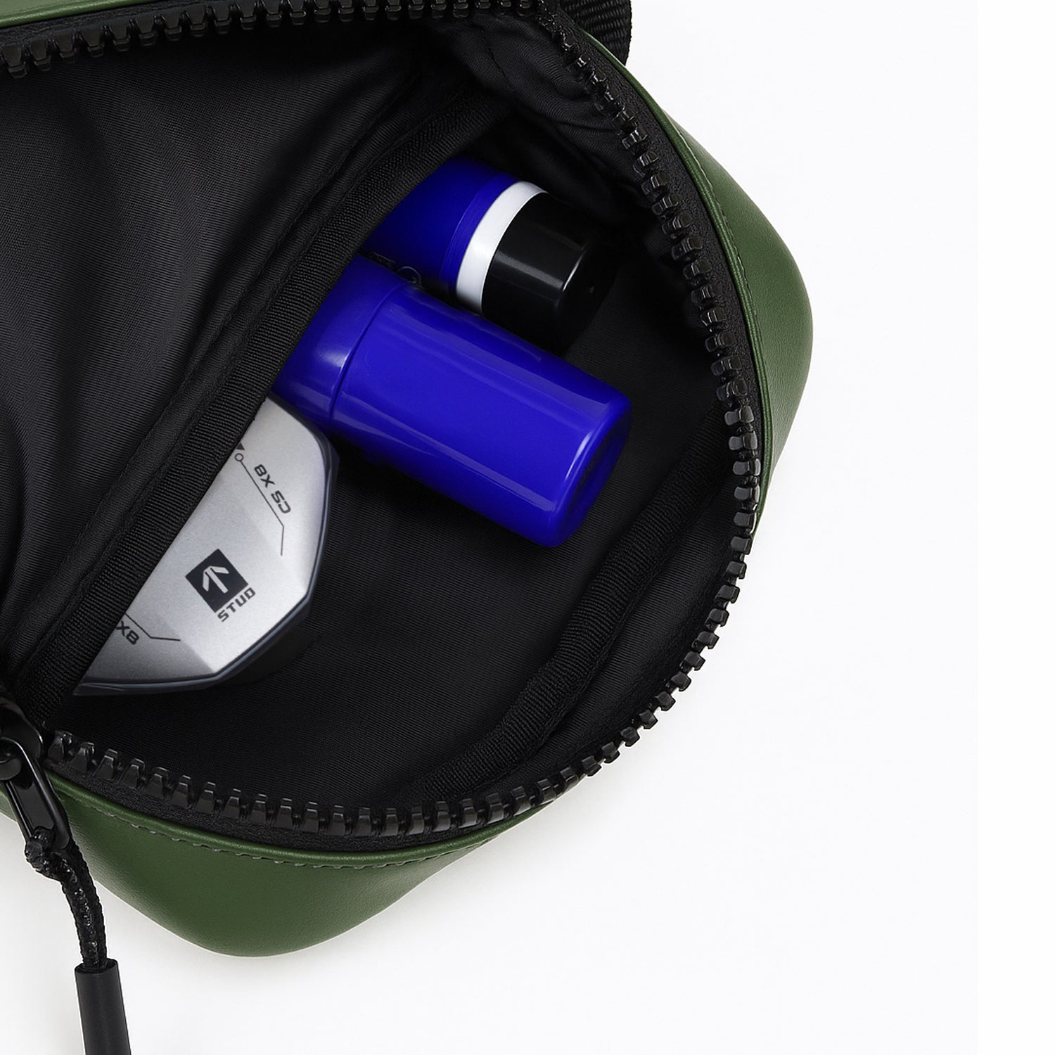 Interior view of The Bloc green bag featuring essential items like a blue bottle and a round compact in the zippered pocket.