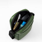 Top view of a stylish green sling bag showcasing organized essentials like a wallet, sunglasses, and a small bottle.