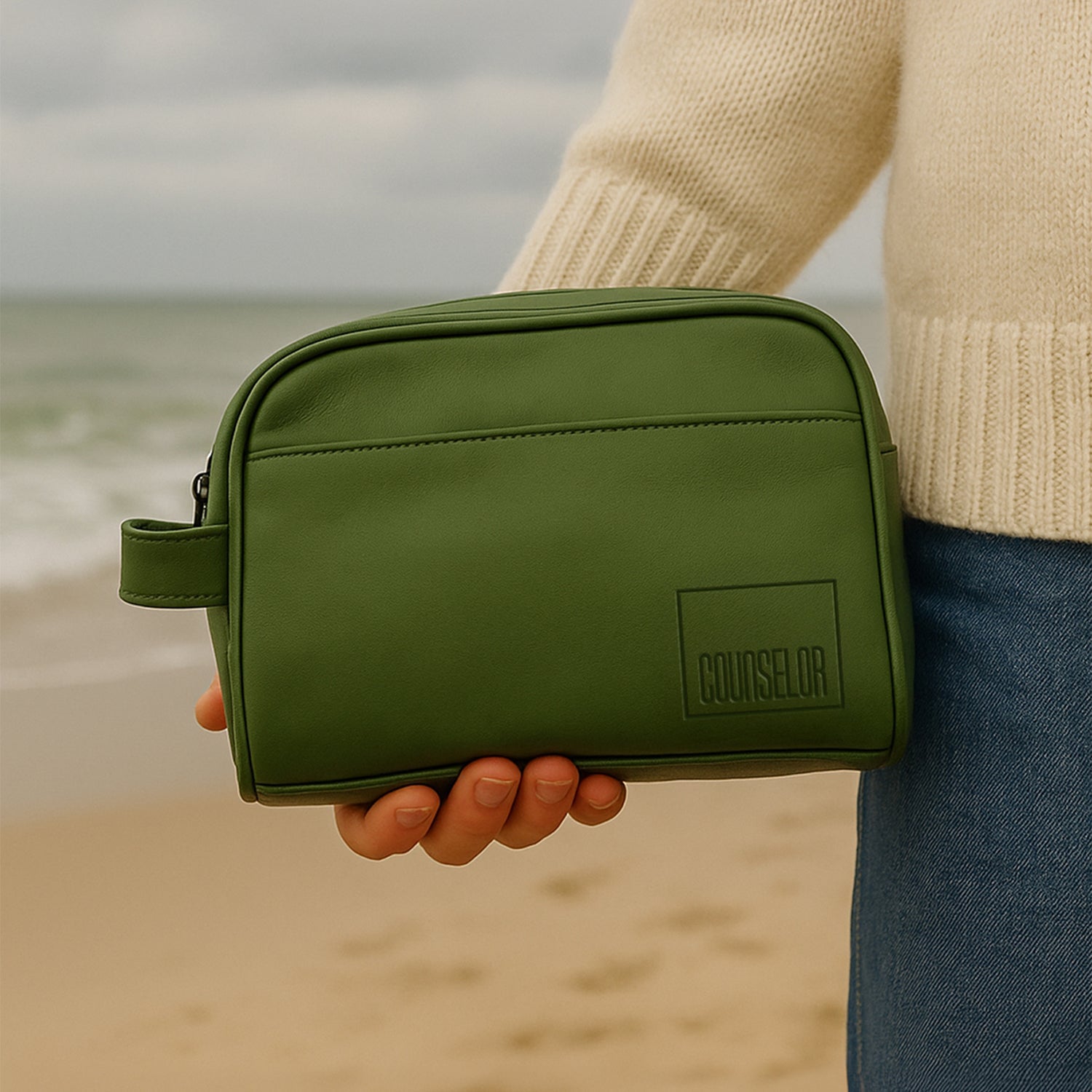 Chic green toiletries kit held by a person on the beach, showcasing eco-friendly vegan leather design.