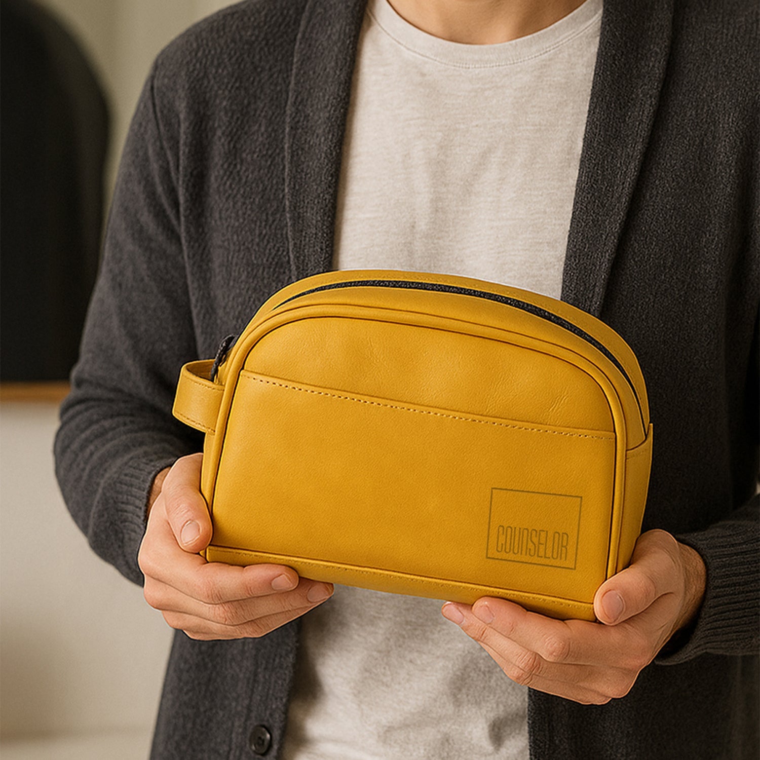 Mustard yellow toiletry bag made from vegan leather, shown being held by a person in a cozy setting.