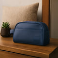 Navy toiletry kit made from vegan leather, showcasing a sleek design on a wooden table with a plant.