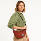 Woman modeling The Zuki rust side sling bag, showcasing its sleek design and adjustable strap.