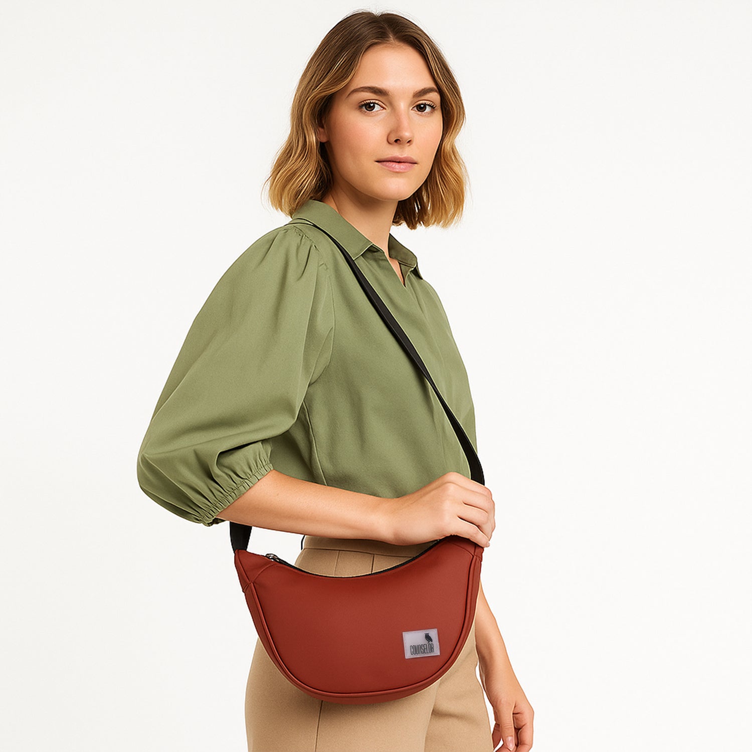 Woman modeling The Zuki rust side sling bag, showcasing its sleek design and adjustable strap.