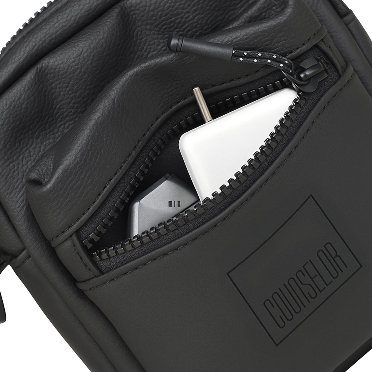 Close-up of NOMA Black bag showing front zipper pocket with tech essentials inside.