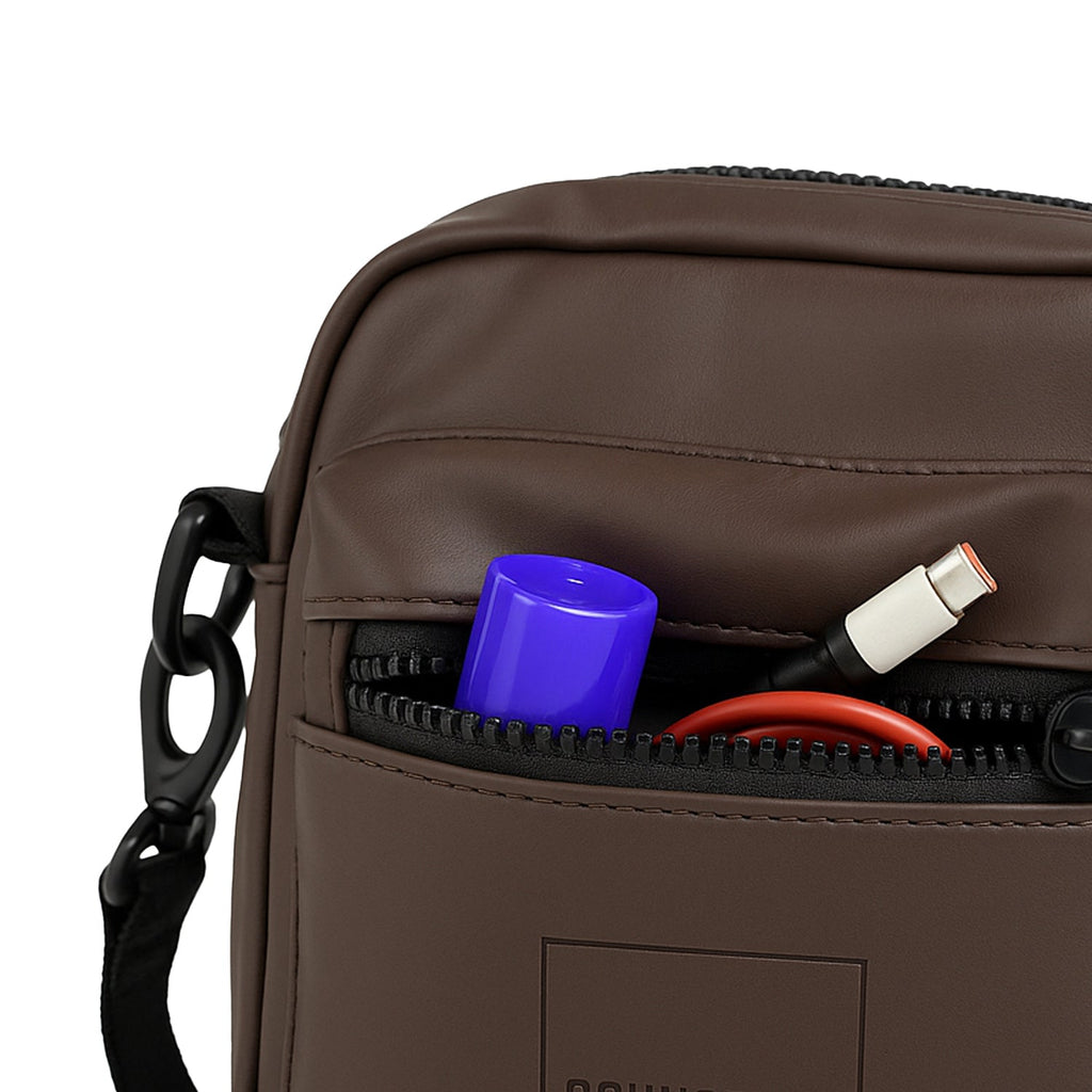 Close-up of the NOMA brown bag's front zipper pocket with pens and accessories visible.