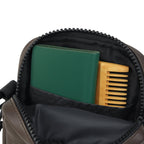 Interior view of The Noma brown bag showing a green notebook and wooden comb in the main compartment.