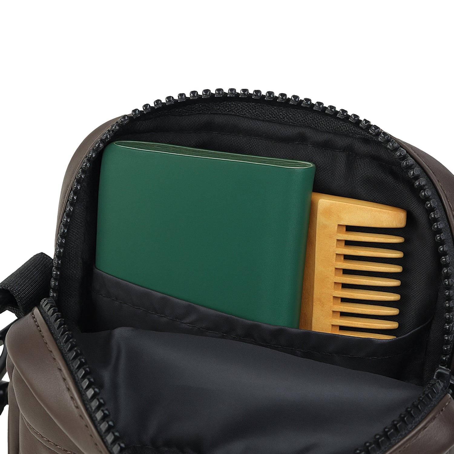 Interior view of The Noma brown bag showing a green notebook and wooden comb in the main compartment.