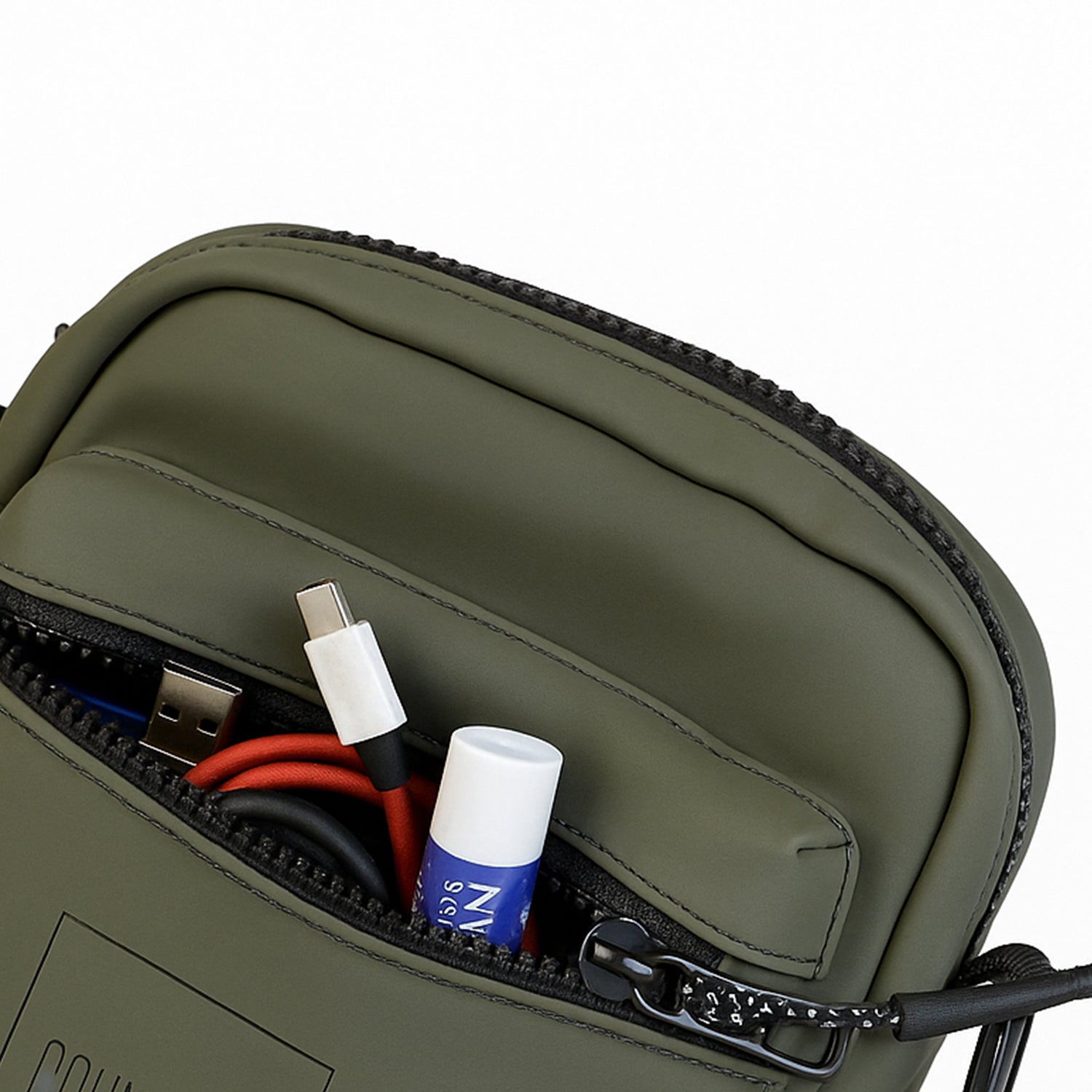 Close-up of The Noma Olive bag's zipper pocket showing organized essentials like cables and lip balm.
