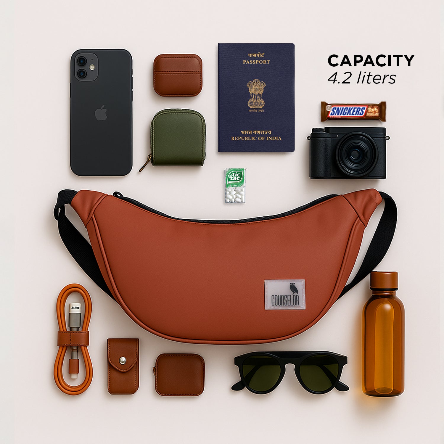 The Zuki rust sling bag surrounded by essential items like a phone, passport, sunglasses, and water bottle.